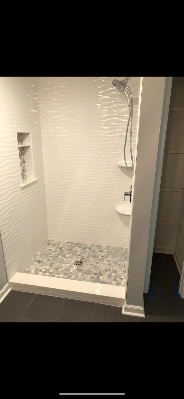 White wavy tile shower with mosaic floor and glass door